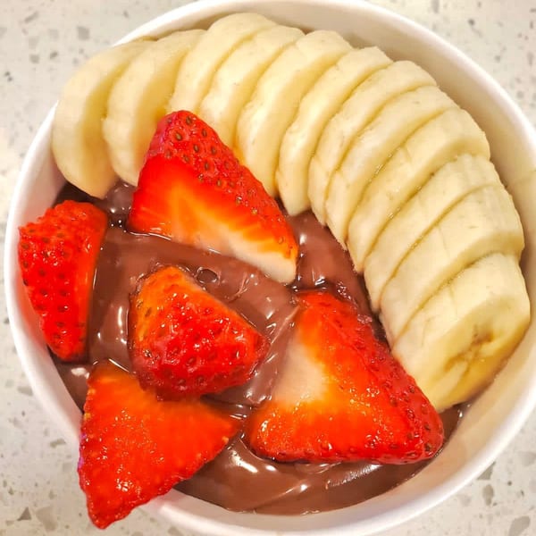 A Sumatra Café chocolate dessert bowl with sliced bananas and strawberries on a white counter.