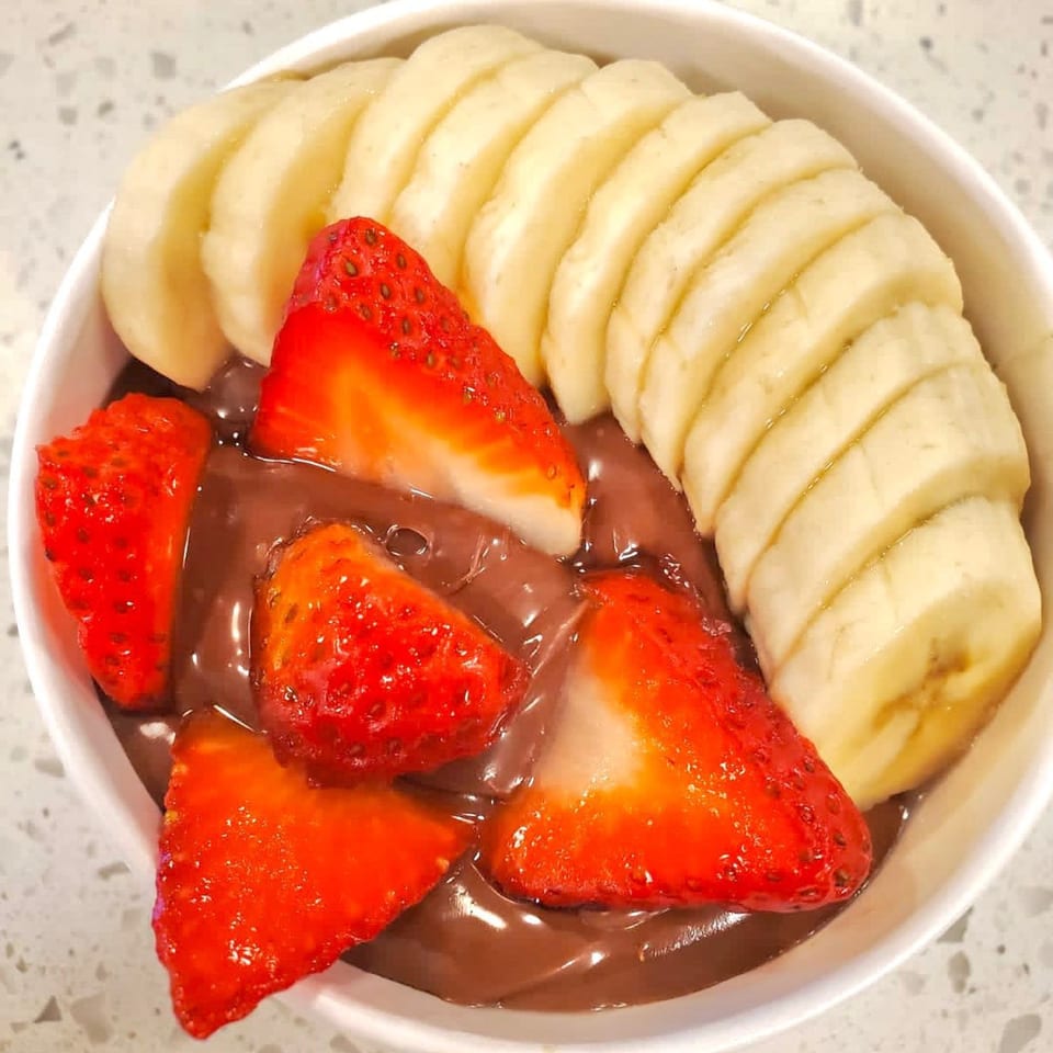 A Sumatra Café chocolate dessert bowl with sliced bananas and strawberries on a white counter.