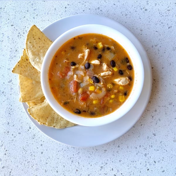 Overhead view of a bowl of Sumatra Café's chicken tortilla soup with tortilla chips on a white plate.