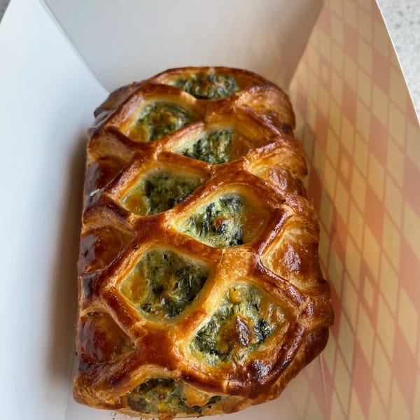Golden-brown pastry with a lattice top revealing green spinach filling, served in a Sumatra Café box.