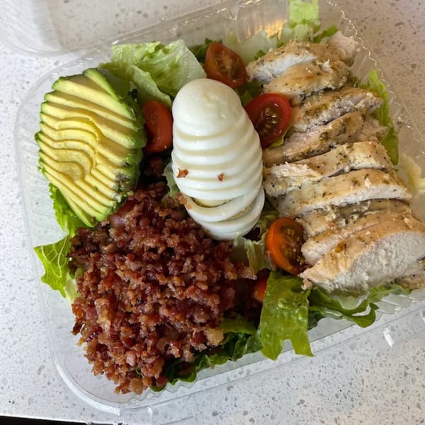 Sumatra Café's Cobb salad with sliced chicken, avocado, bacon, egg, and tomatoes in a plastic container.