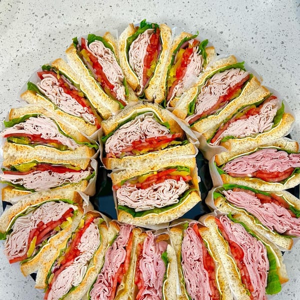 A platter of Sumatra Café sandwiches, cut in half, showcasing deli meat, lettuce, and tomatoes.
