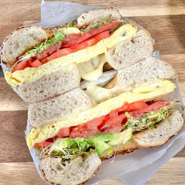 A Sumatra Café bagel sandwich, cut in half, filled with egg, cheese, tomatoes, and sprouts.